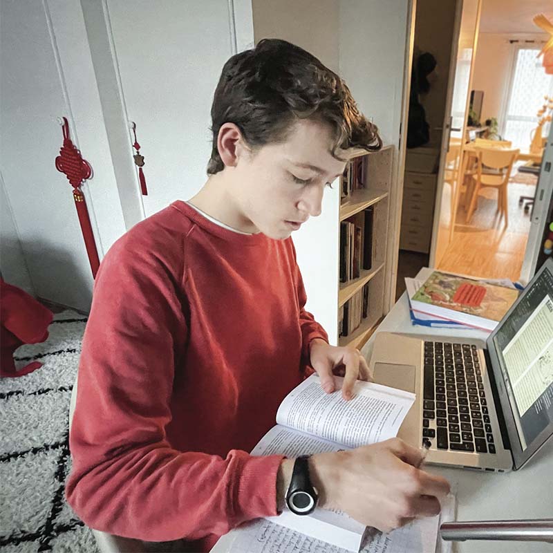Adrien en train de réaliser son journal, avec un ordinateur et des documents.